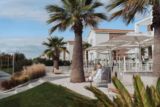 Vista laterale della Clubhouse di Pareus Beach con palme, prato e ciottoli. Donna su un lettino