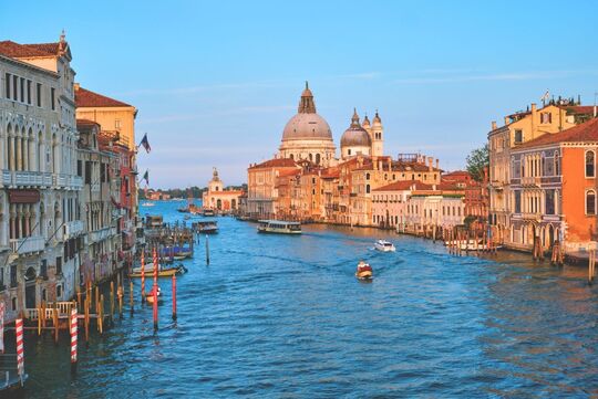 View of Venice canals with colorful houses, gondolas on the water, and the Duomo in the background – iconic Venetian scenery.