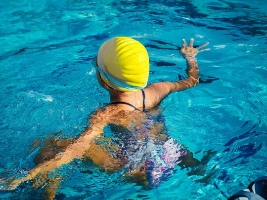 Girl with yellow swimming cap in the water from behind. Swimming fun in Caorle's indoor pool.
