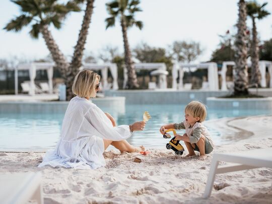 Mom and child enjoying the beach area of the pool at Pareus Beach Resort – relaxed family time by the sea.